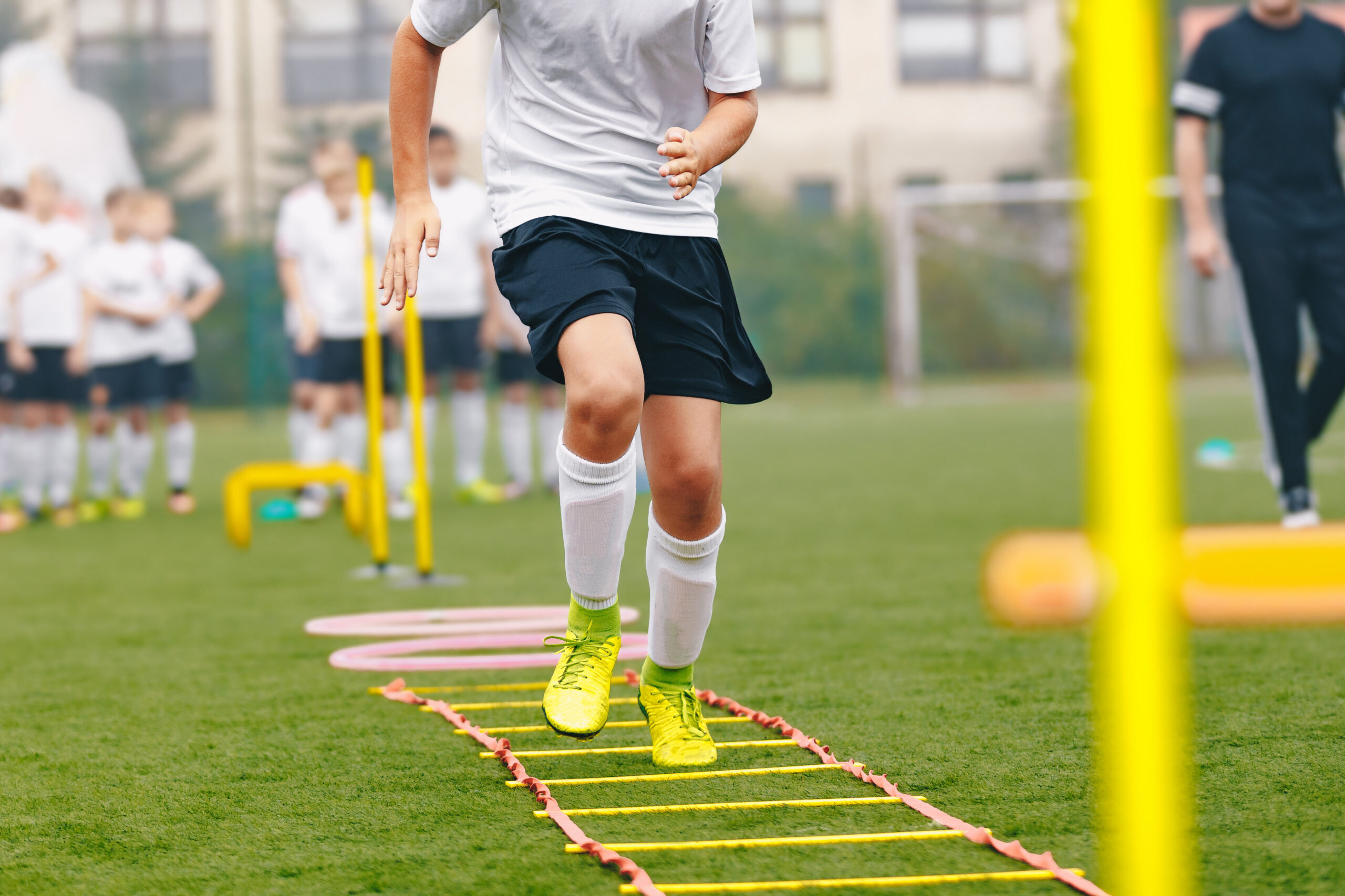 Junge Fußballspieler*innen trainieren mit Koordinationsleiter auf dem Rasen.
